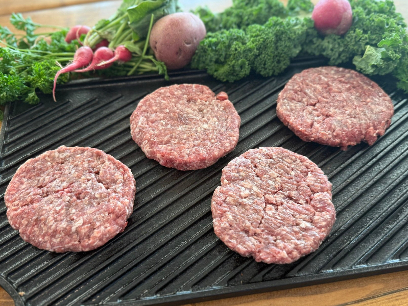 Raw ground beef hamburger patties on a grill pan with fresh vegetables on a wooden surface