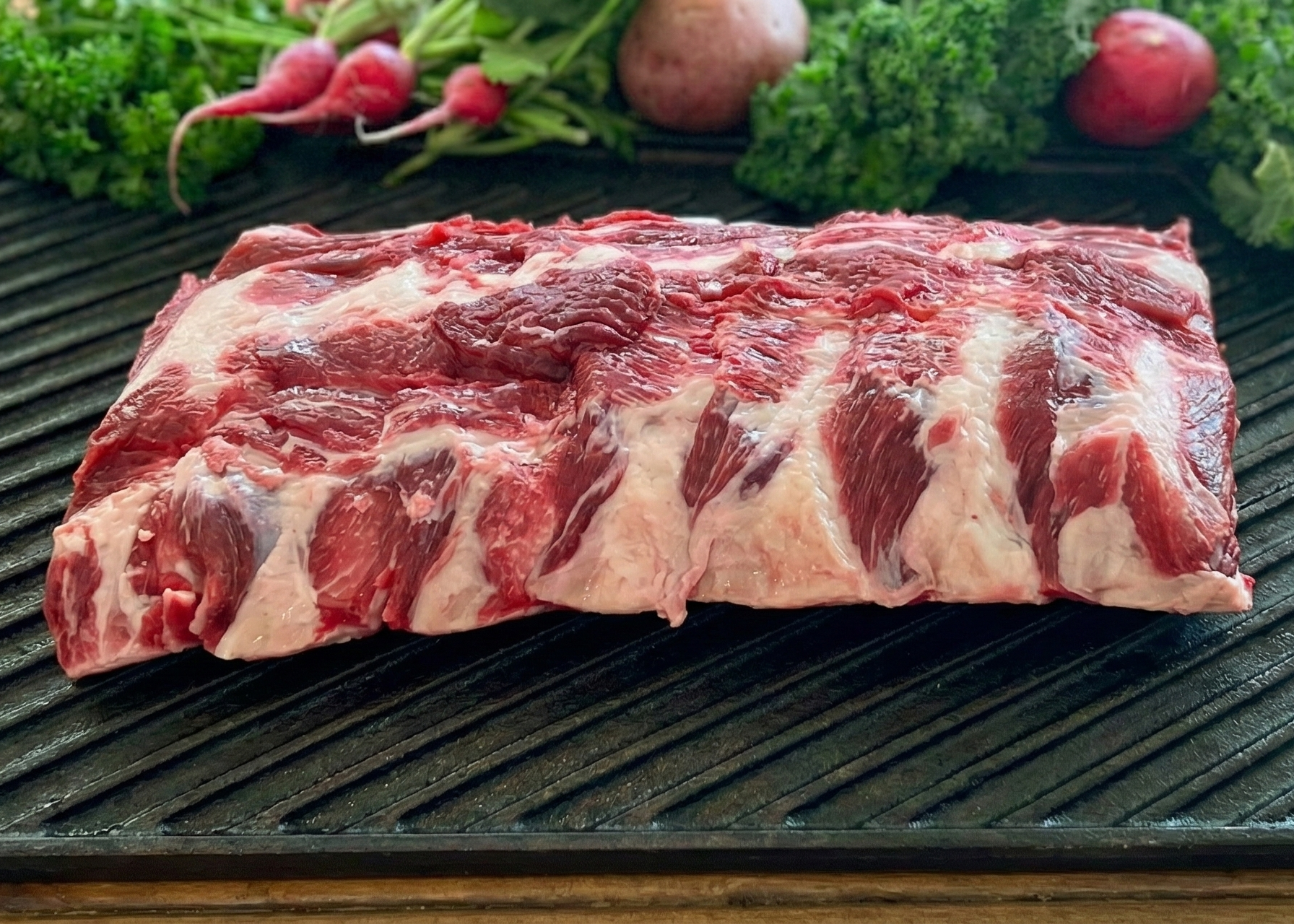 Beef Baby Back Ribs on a grill pan with vegetables on a wooden surface
