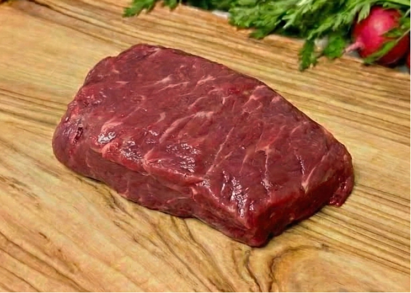 Beef Boneless Bonanza Steak on a wooden cutting board with vegetables in the background