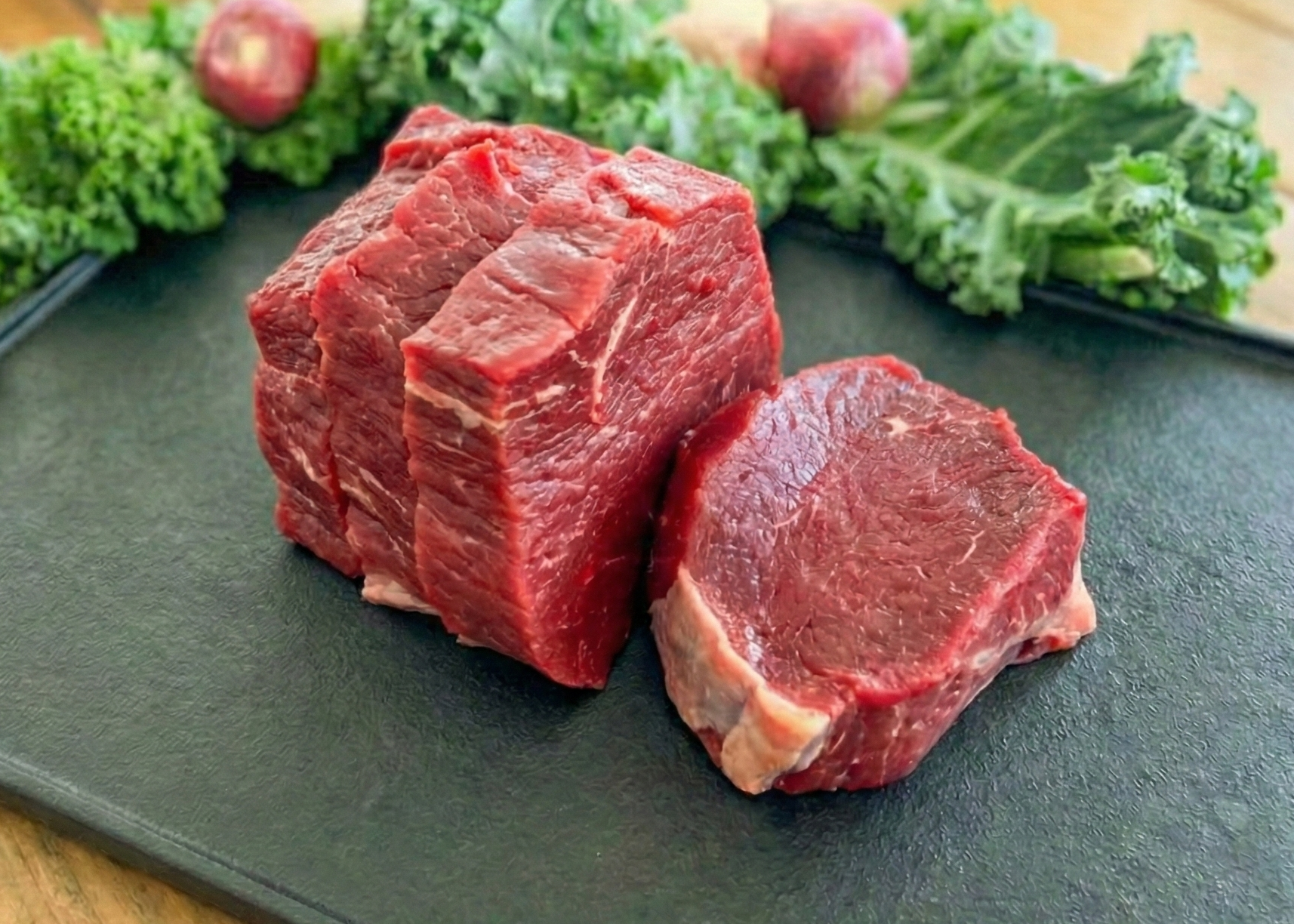 Beef Eye of Round Steak on a green cutting board with kale and apples in the background.