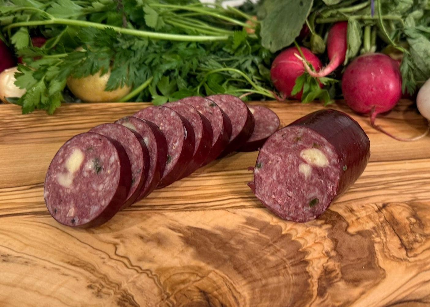 Beef Jalapeño and Cheese Summer Sausage on a wooden cutting board with fresh vegetables in the background.