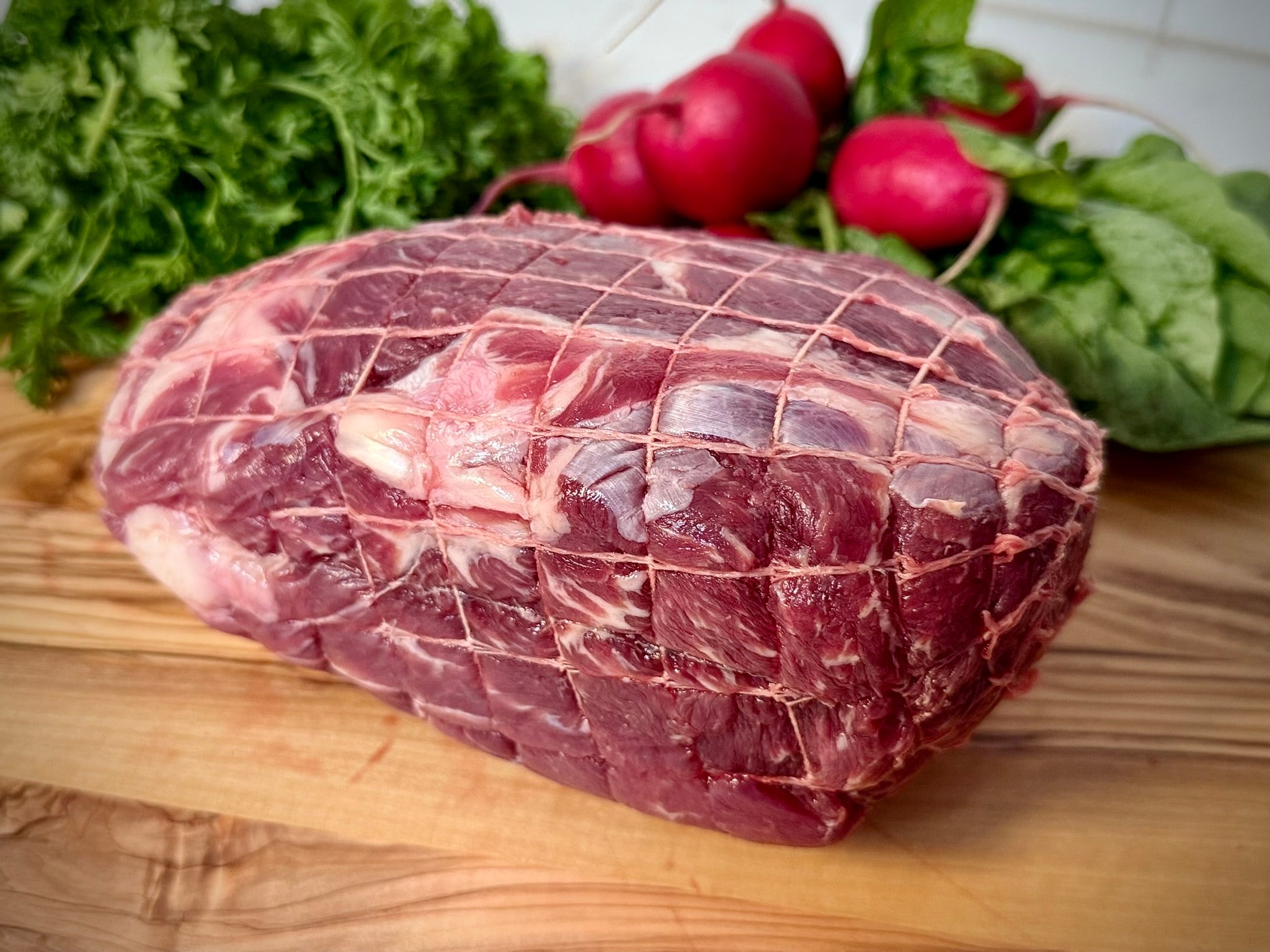 Beef Premium Sirloin Roast (Small) on a wooden cutting board with vegetables in the background