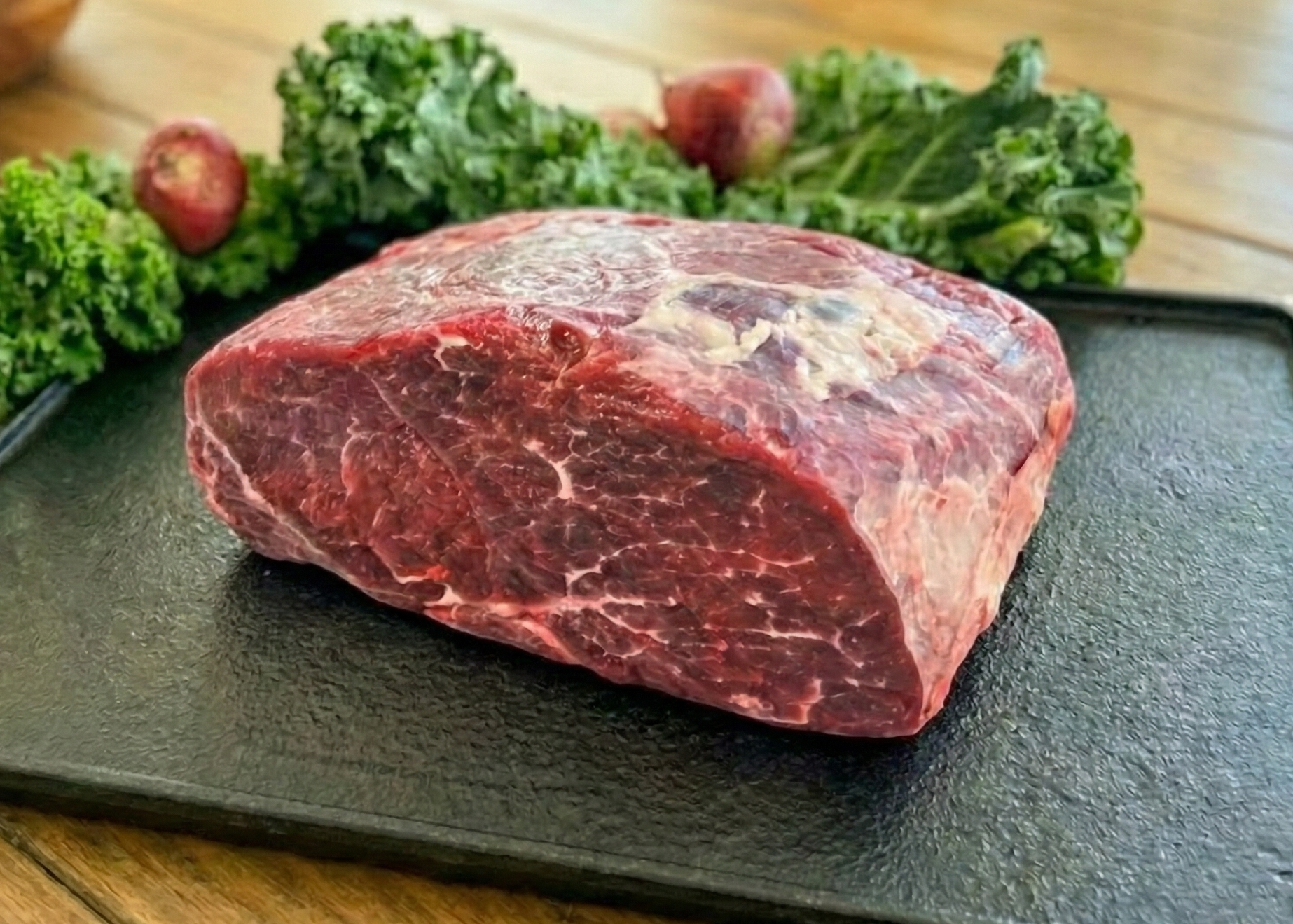 Beef Sirloin-Tip Roast on a black tray with greens on a wooden surface