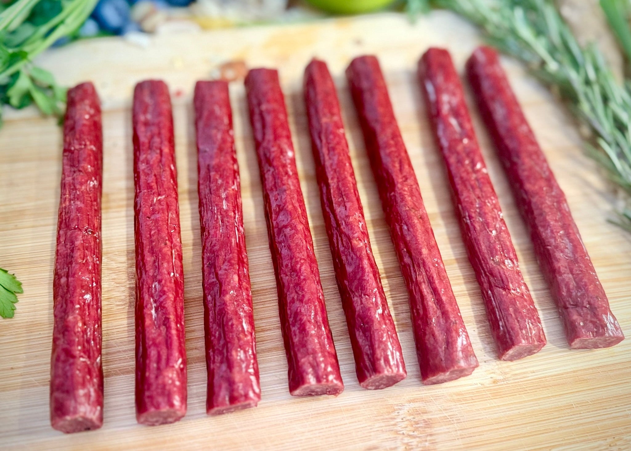 Beef Sticks sticks on a wooden cutting board with herbs in the background