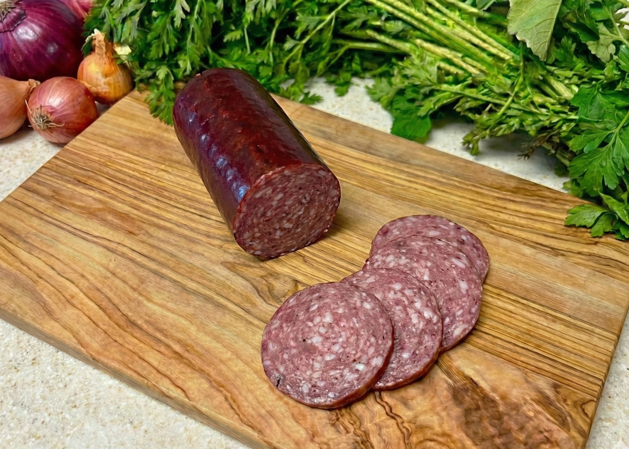 Beef Uncured Summer Sausage on a wooden cutting board with fresh herbs and onions in the background.