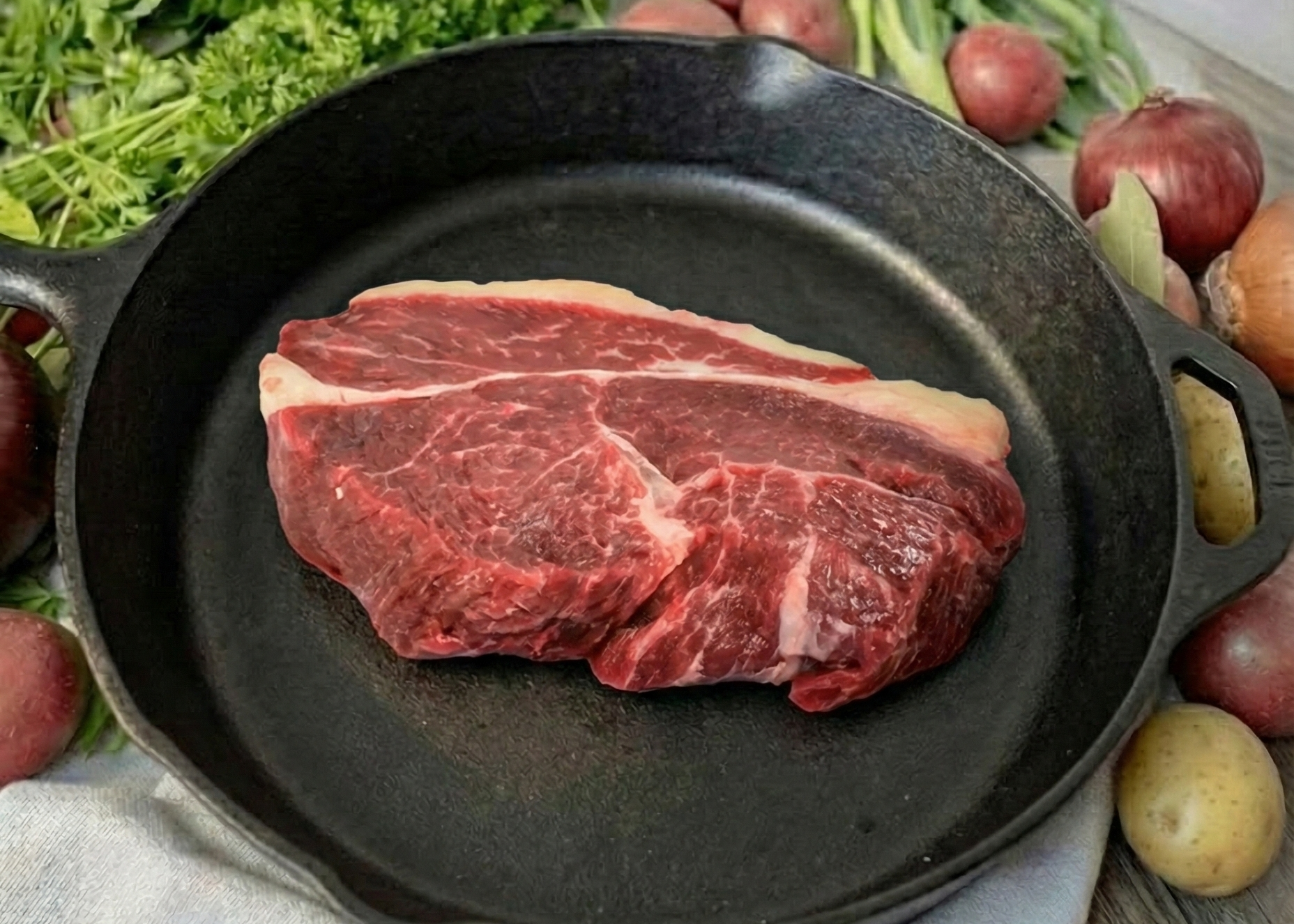 Boneless Beef Sirloin Steak in a black skillet surrounded by fresh vegetables on a wooden surface