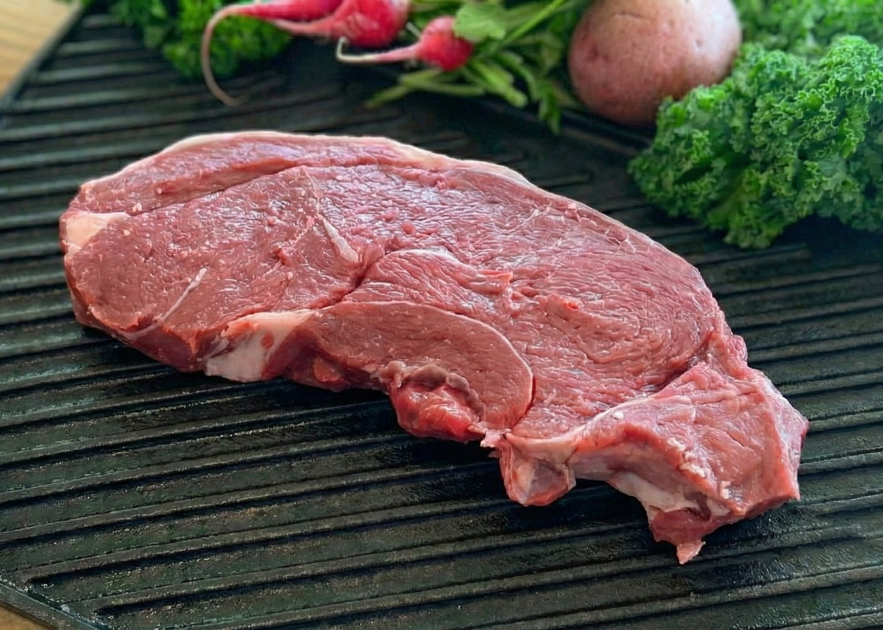 Raw Boneless Buffalo Sirloin Steak on a grill pan with vegetables on a wooden surface