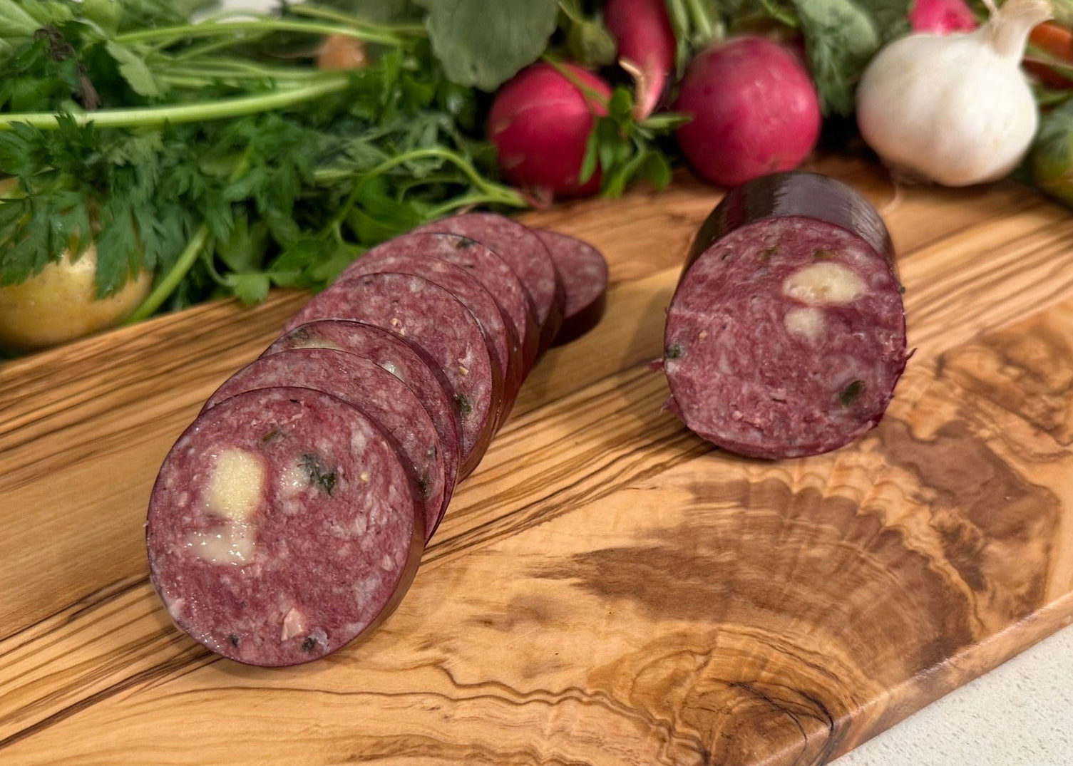 Buffalo Jalapeno/Cheese Summer Sausage on a wooden cutting board with vegetables in the background