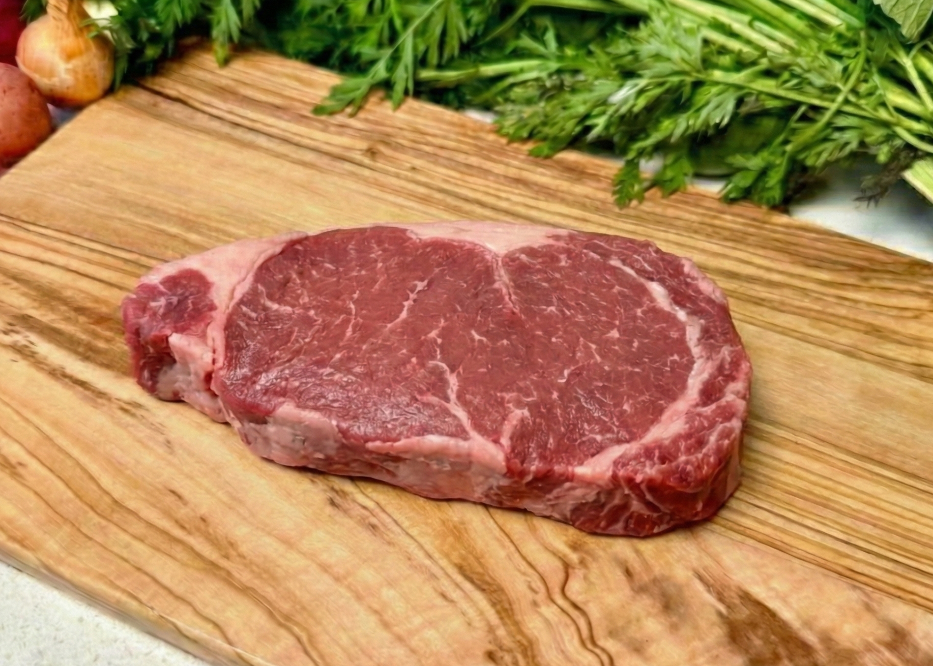 Buffalo New York Strip Steak on a wooden cutting board with vegetables in the background