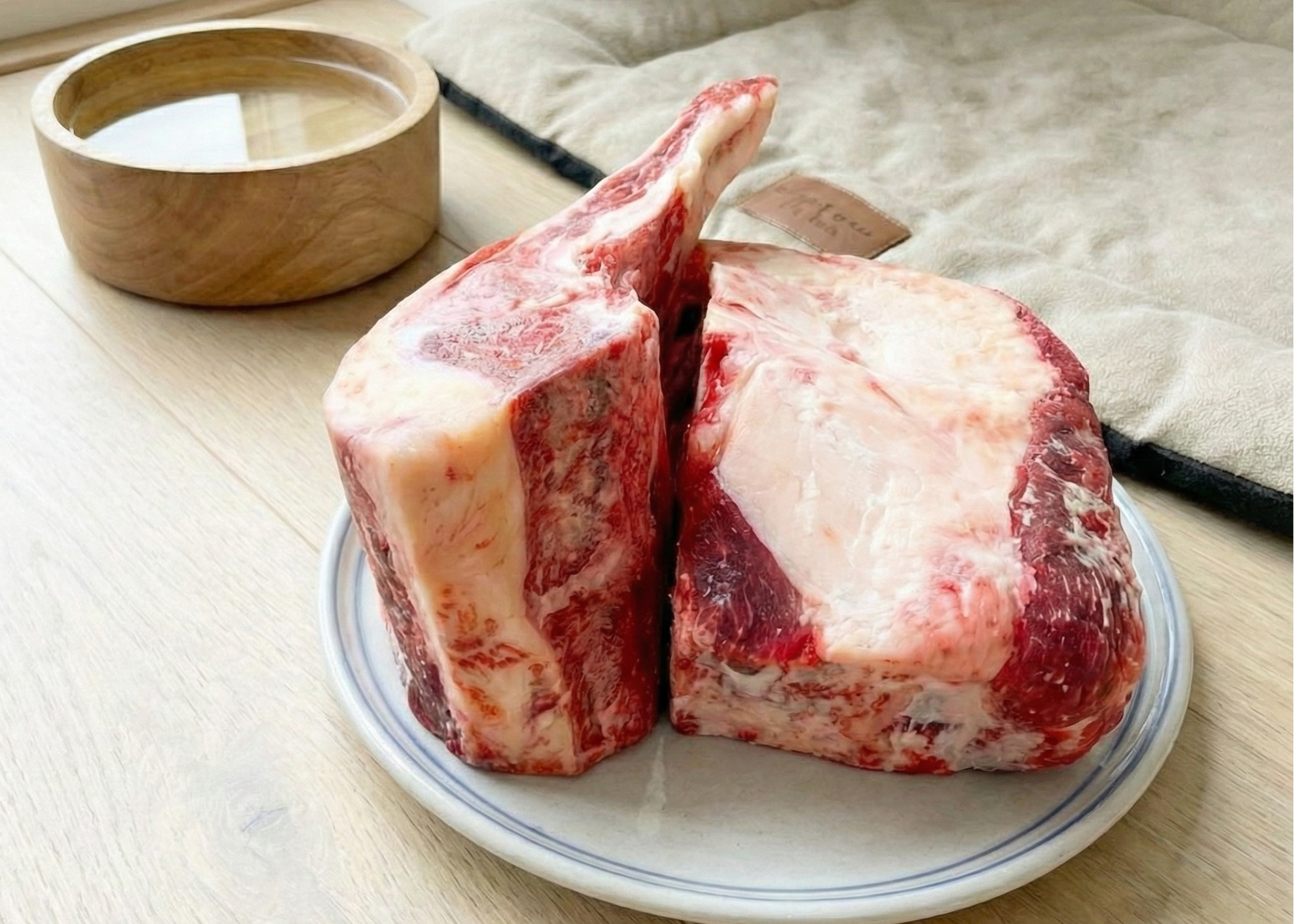 Two Dog Beef Brisket Bones on a white plate with a wooden bowl in the background.