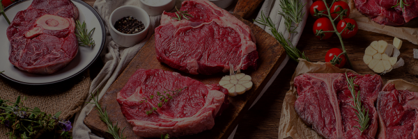 Raw steak on a wooden cutting board with vegetables and spices.