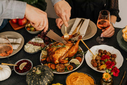People enjoying a meal around a table with roasted chicken, vegetables, and drinks.