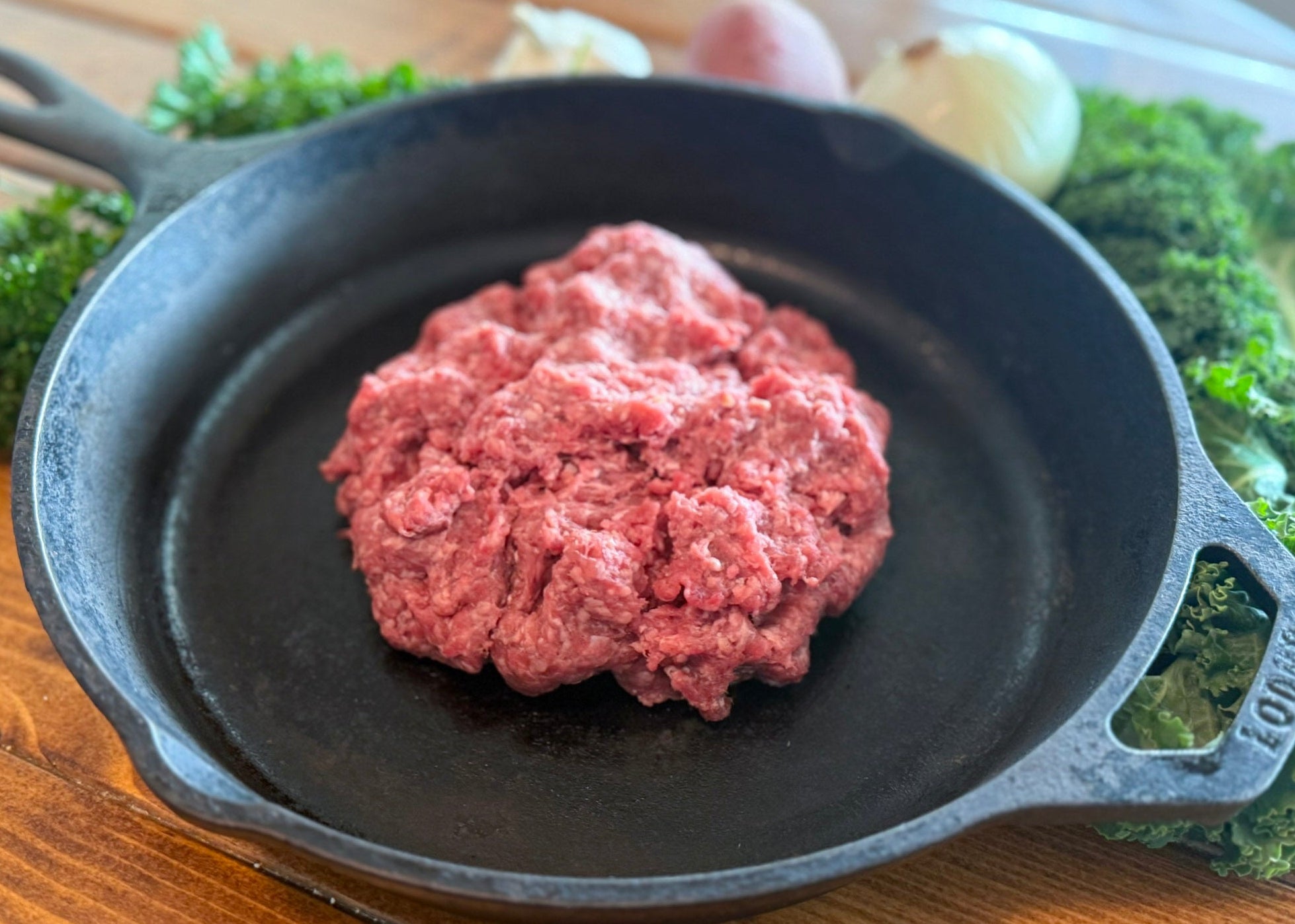 Ground Beef 10% Fat Small Pack in a cast iron skillet on a wooden surface with greenery in the background