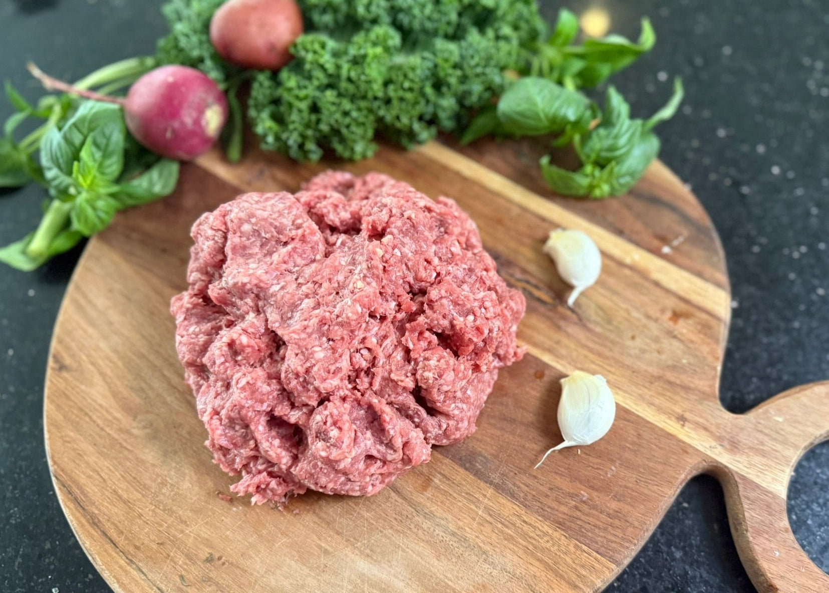 Ground Beef High Fat 78/22 (Small) on a wooden cutting board with vegetables in the background