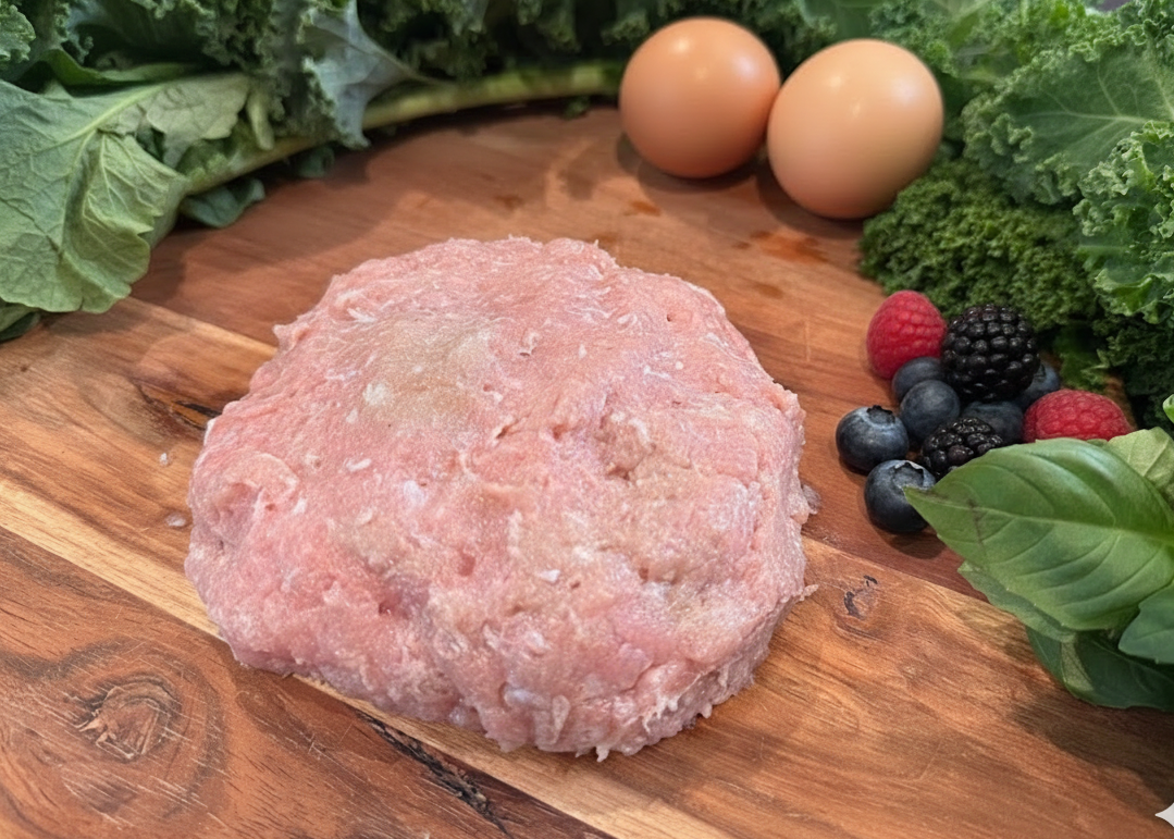 Raw ground Chicken Breakfast Sausage on a wooden cutting board with eggs, berries, and greens.
