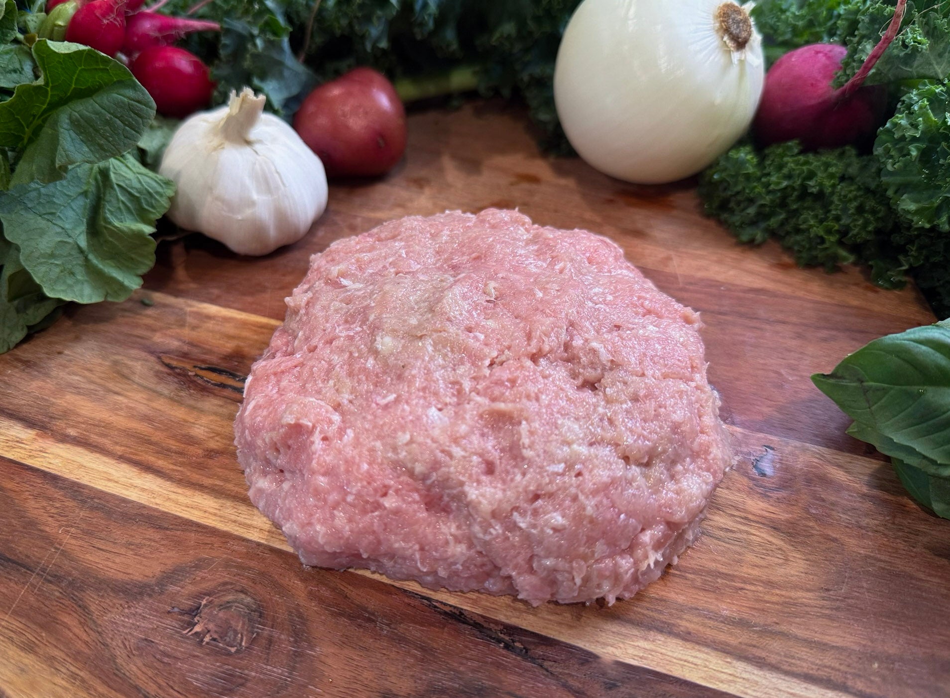 Raw ground pork on a wooden cutting board with vegetables in the background