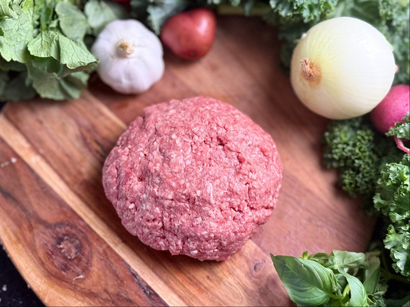 Raw ground meat patty on a wooden board with vegetables