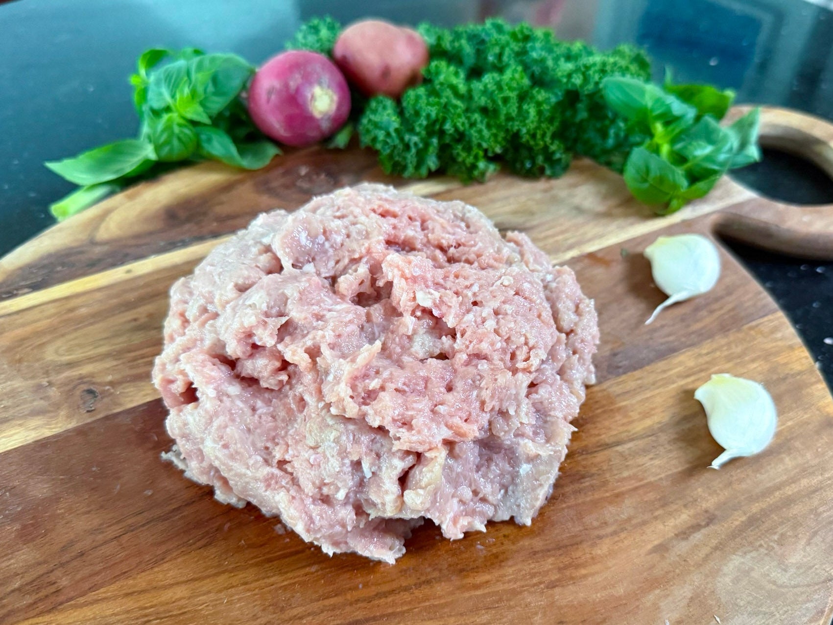 Raw ground pork on a wooden cutting board with vegetables in the background