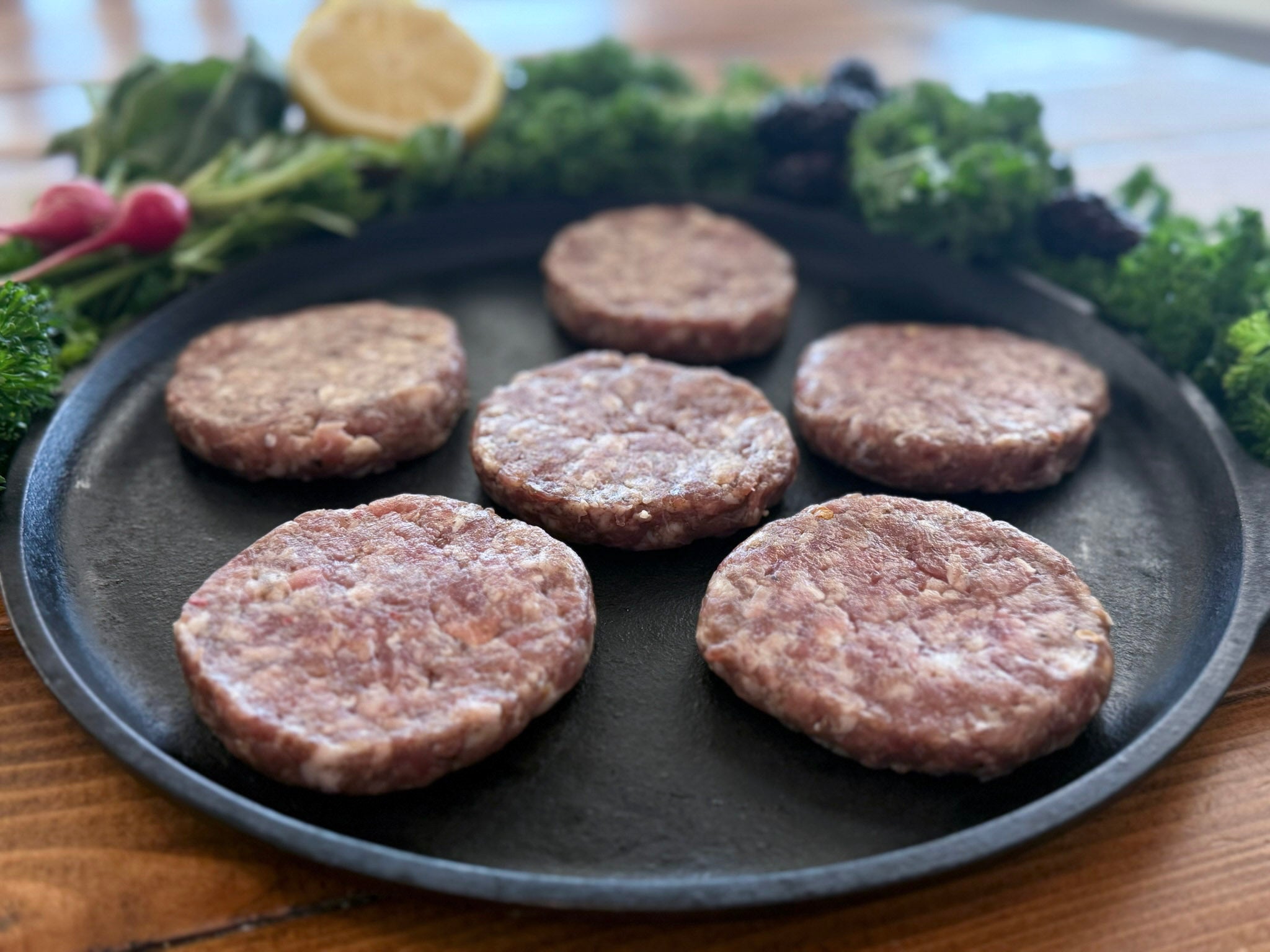 Raw sausage patties on a black plate with vegetables in the background
