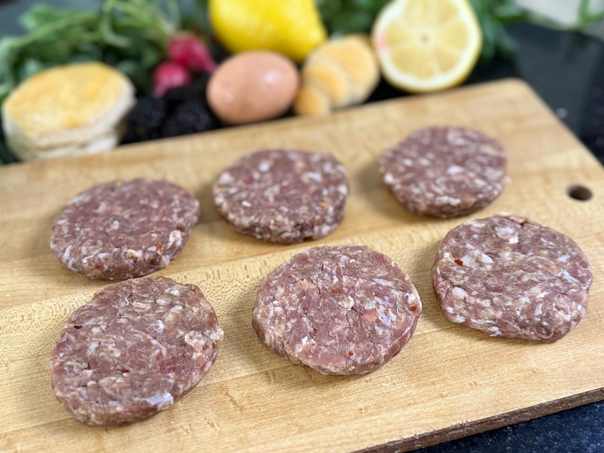 Raw sausage patties on a wooden cutting board with vegetables in the background