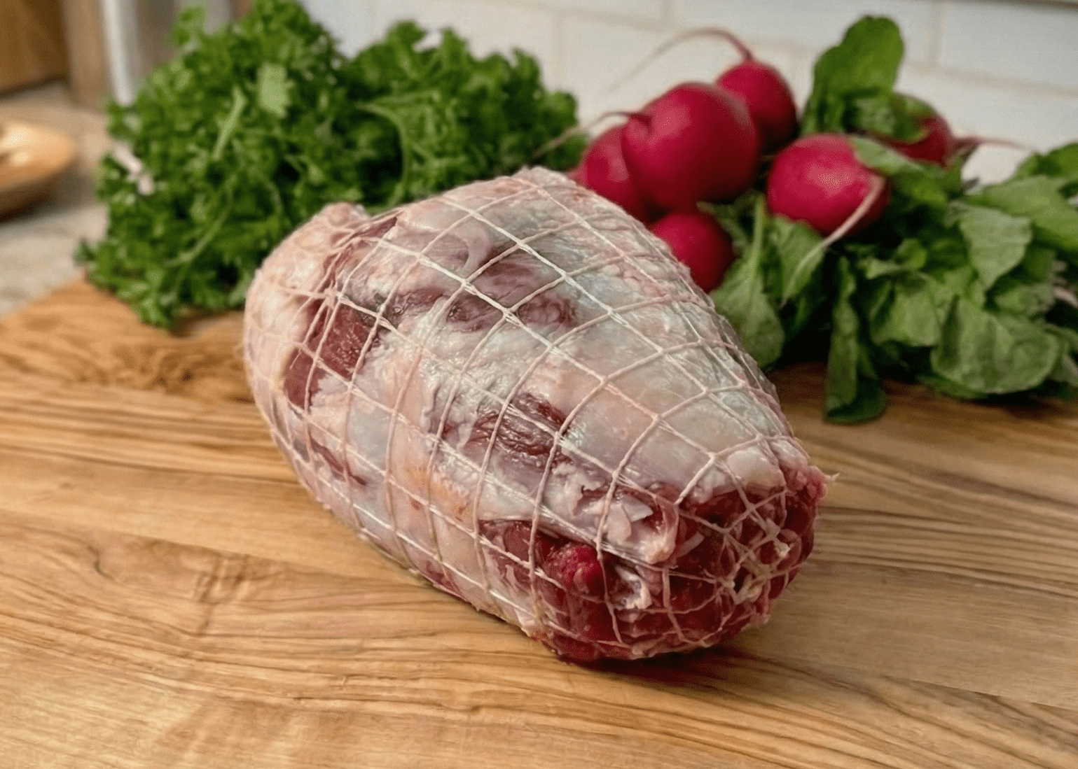 Leg of Lamb (Boneless) on a wooden cutting board with vegetables in a kitchen setting