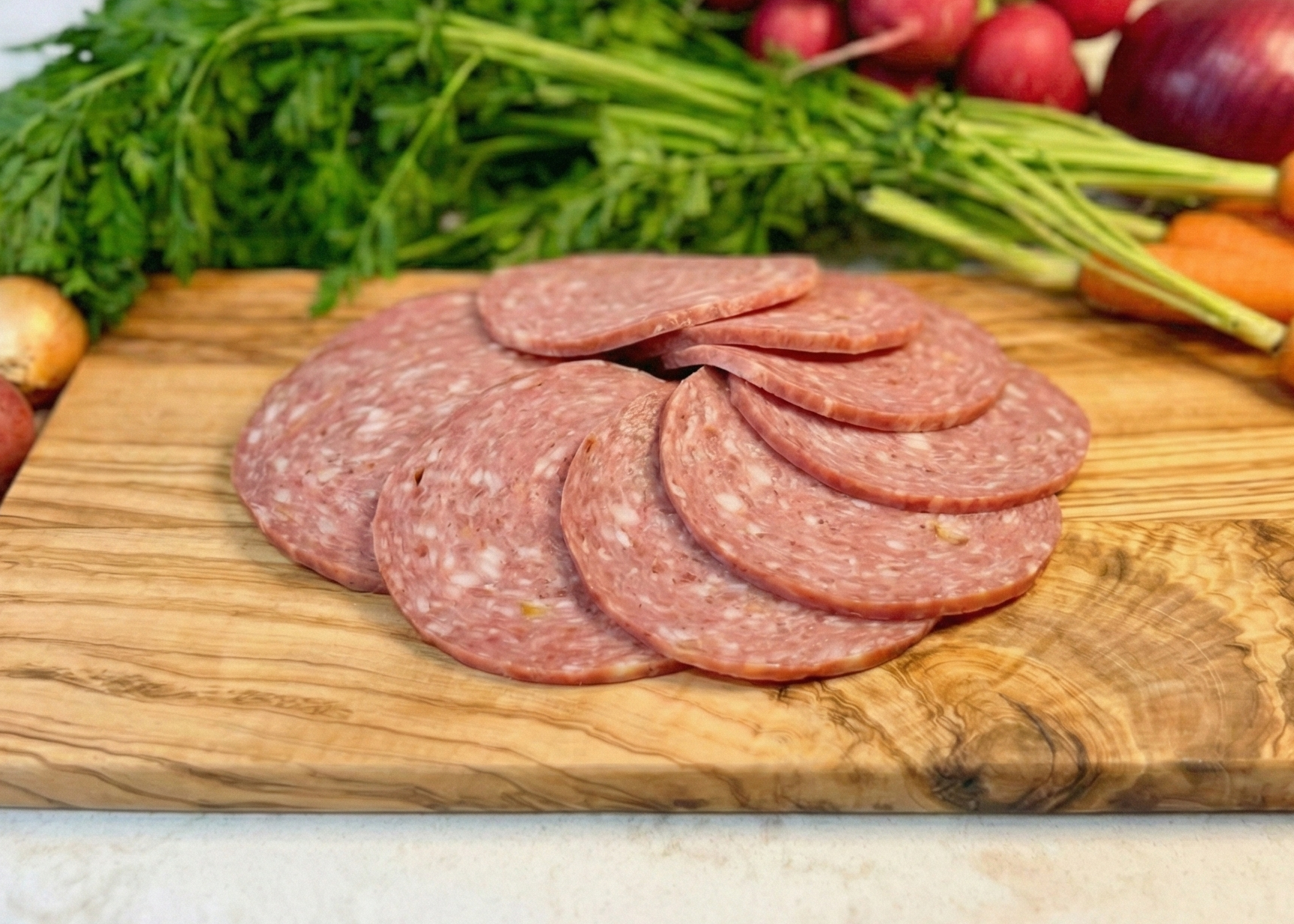 Sliced pepperoni on a wooden cutting board with vegetables in the background