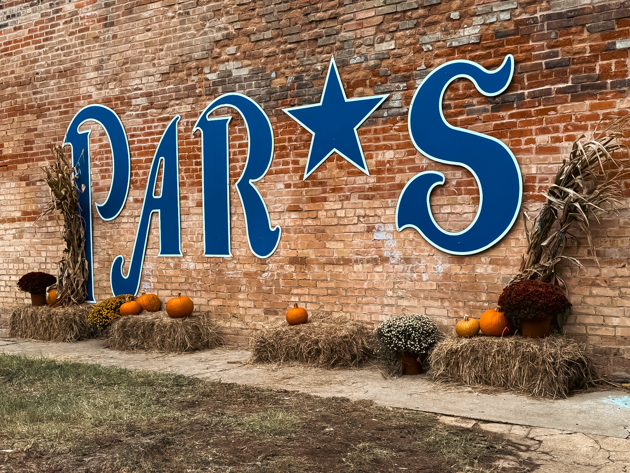 Brick wall with large blue letters Paris and pumpkins on hay bales.