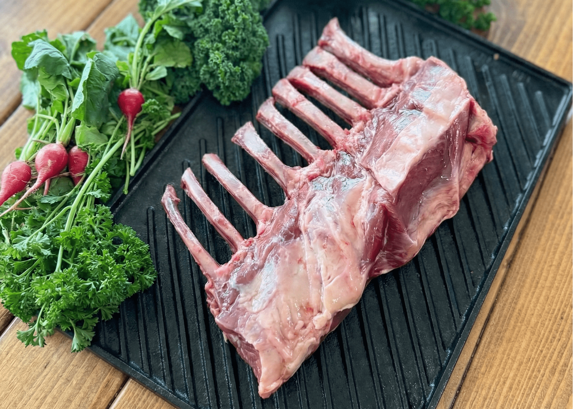 Raw pasture raised lamb rack on a grill pan with vegetables on a wooden surface