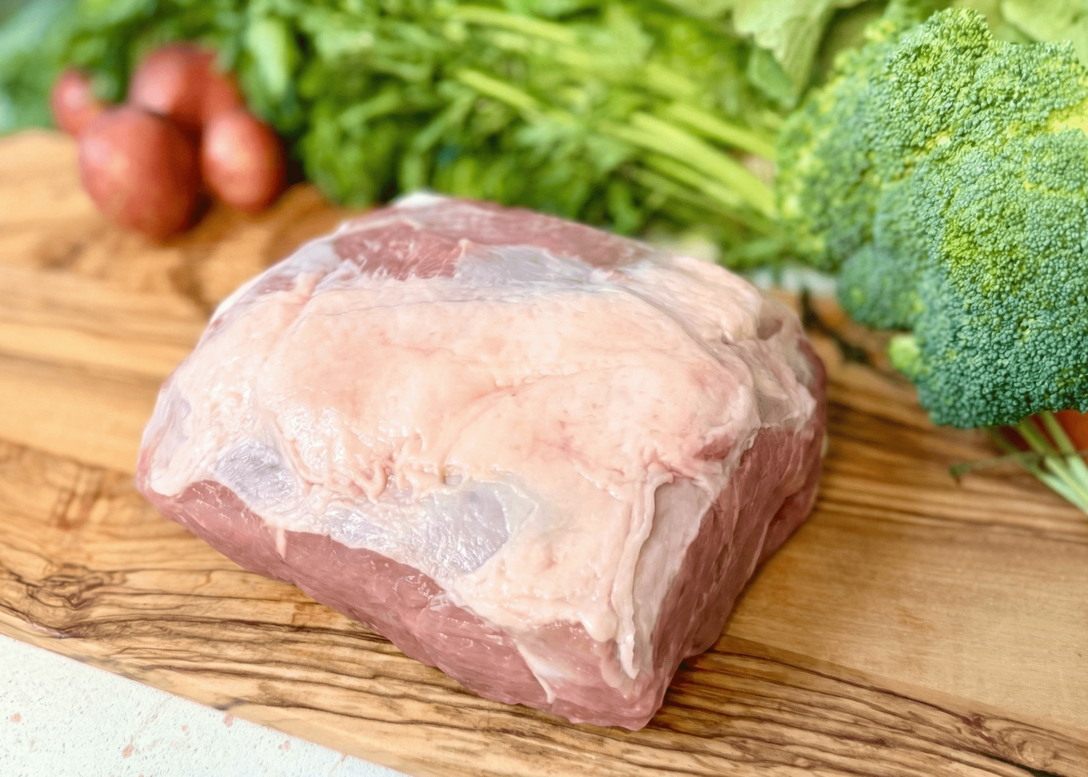 Raw Pork Boston Butt Roast on a wooden cutting board with vegetables in the background
