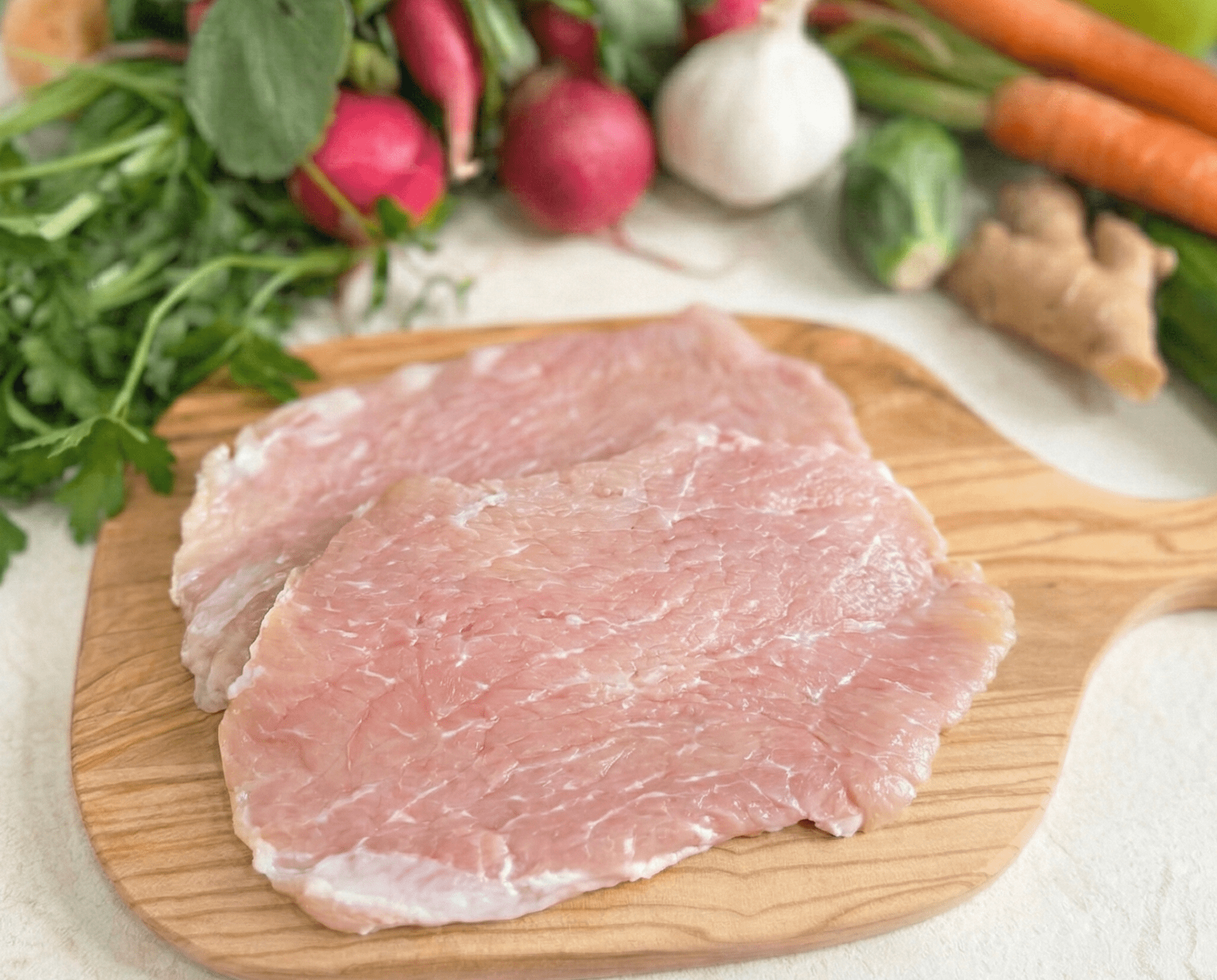 Pork Cutlets on a board with vegetables behind the Cutlets
