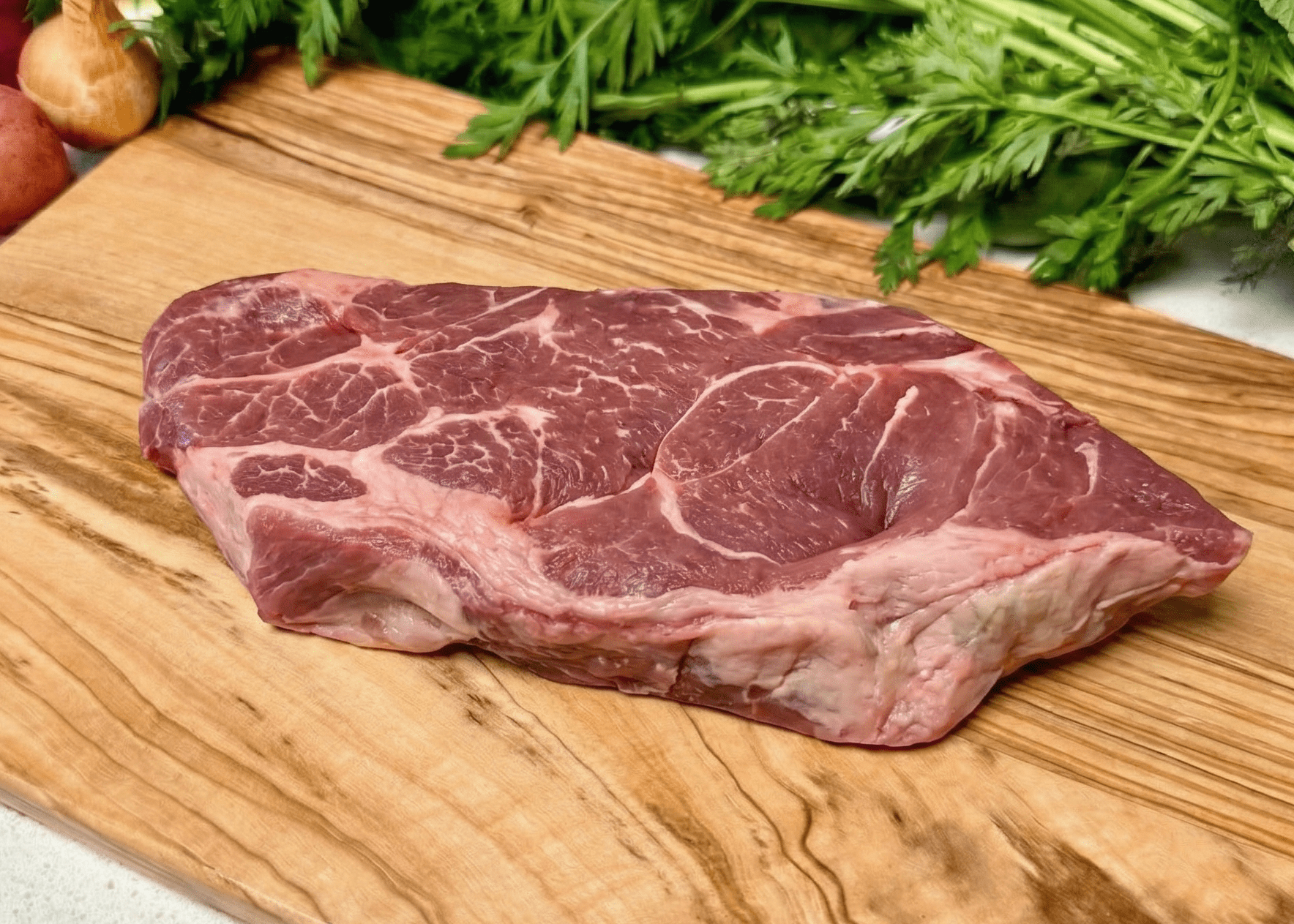 Raw Pork Shoulder Steak on a wooden cutting board with vegetables in the background