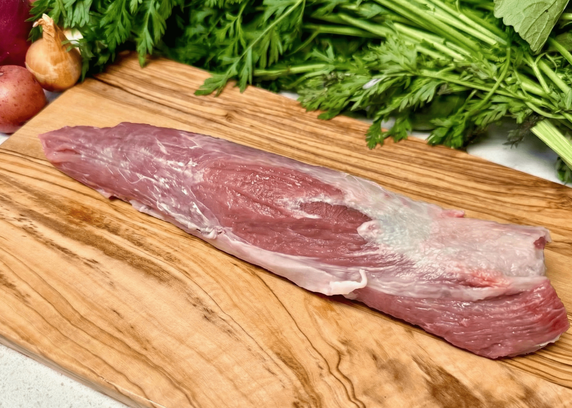 Raw Pork Tenderloin on a wooden cutting board with vegetables in the background