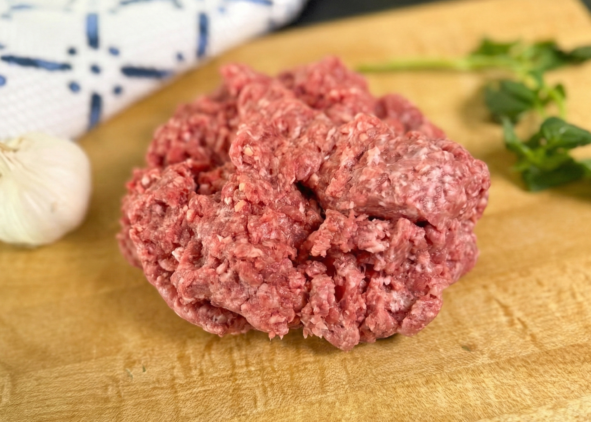 Primal Ground Beef on a wooden cutting board with herbs and garlic.