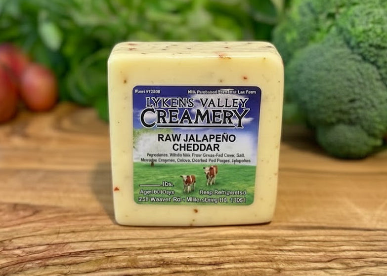 Block of Lykens Valley Creamery Raw Jalapeno Cheddar cheese on a wooden cutting board with vegetables in the background.