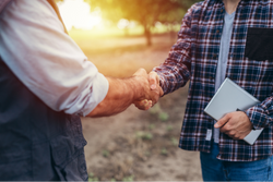 Two people shaking hands outdoors with a blurred background