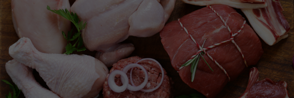 Assorted meats including chicken legs, salami, and ham on a wooden surface.