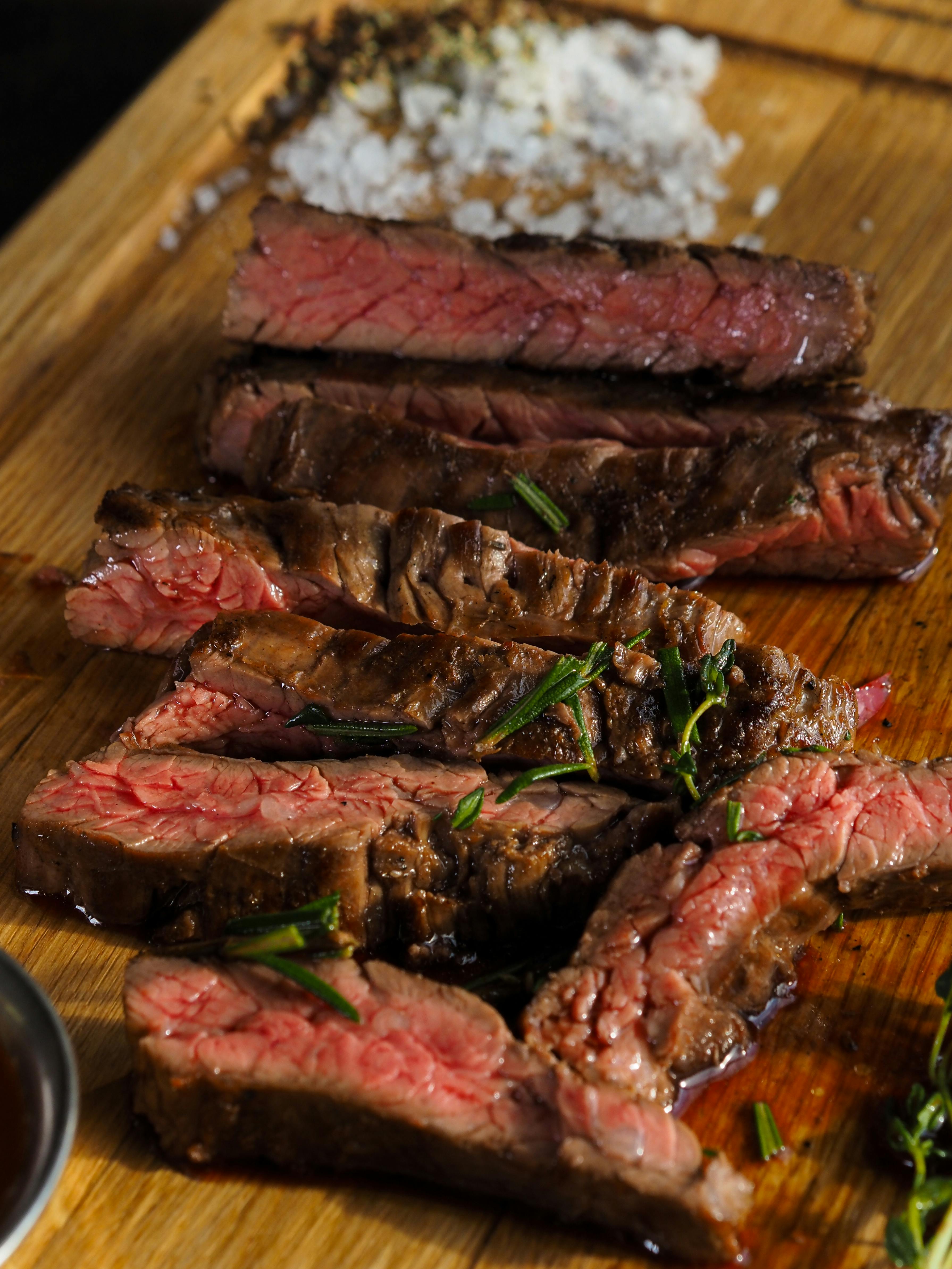 Sliced steak on a wooden cutting board with salt and herbs.