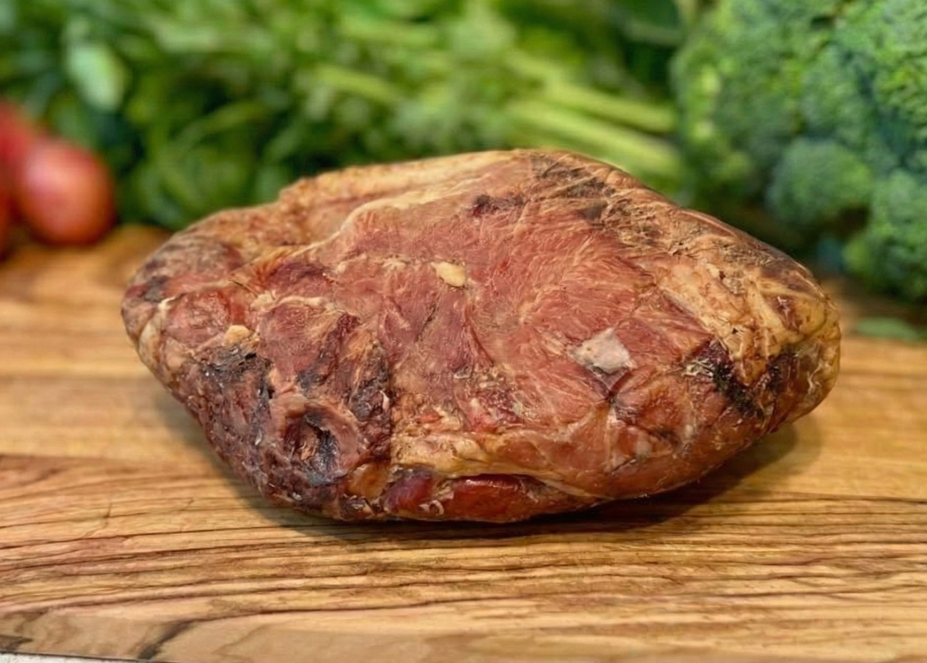 Raw Smoked Ham Steak Ends on a wooden cutting board with vegetables in the background