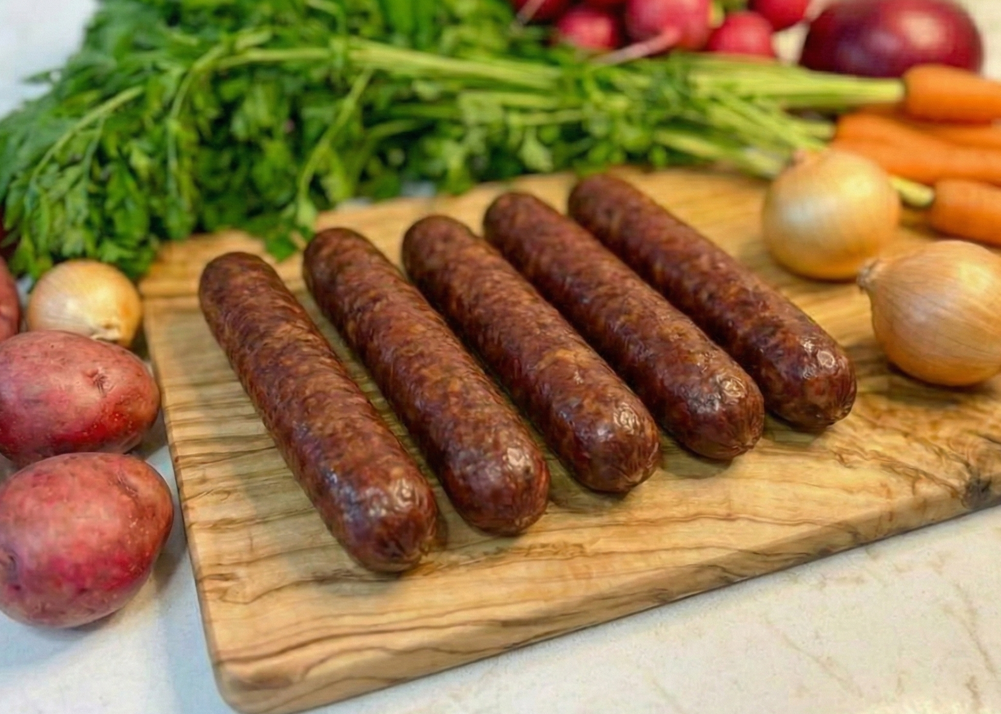 Wooden cutting board with Smoked Pork Bratwursts, surrounded by vegetables on a light surface