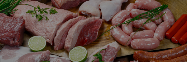 Assorted raw meats including sliced pork, chicken, and sausages on a wooden board with limes and rosemary.