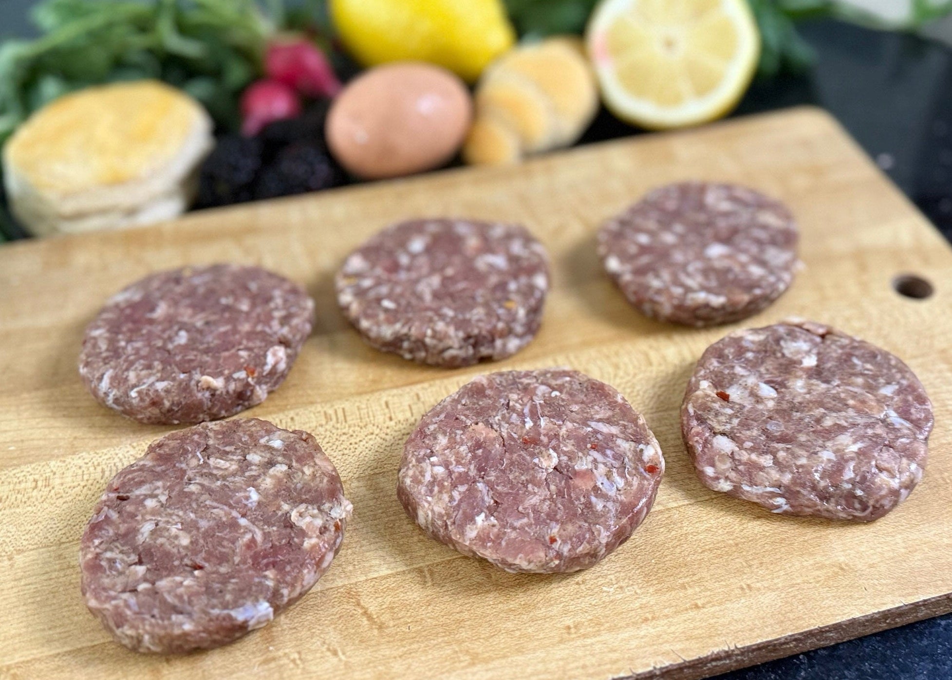 Raw sausage patties on a wooden cutting board with vegetables in the background