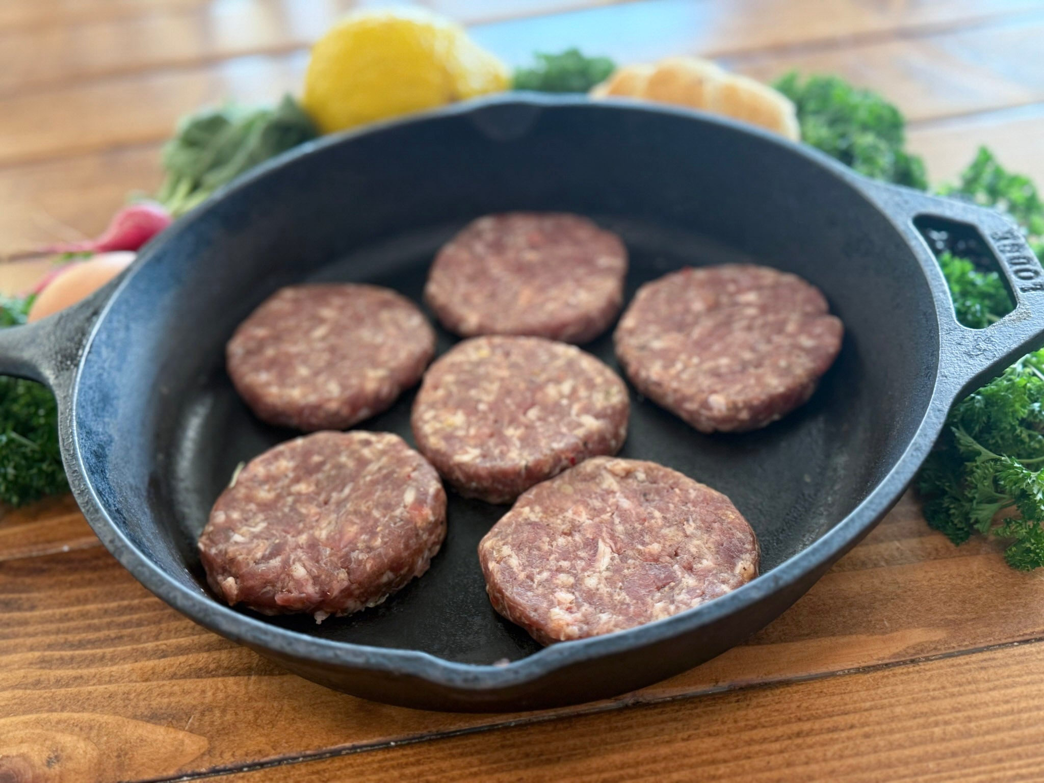 Raw breakfast patties in a cast iron skillet on a wooden surface with vegetables.