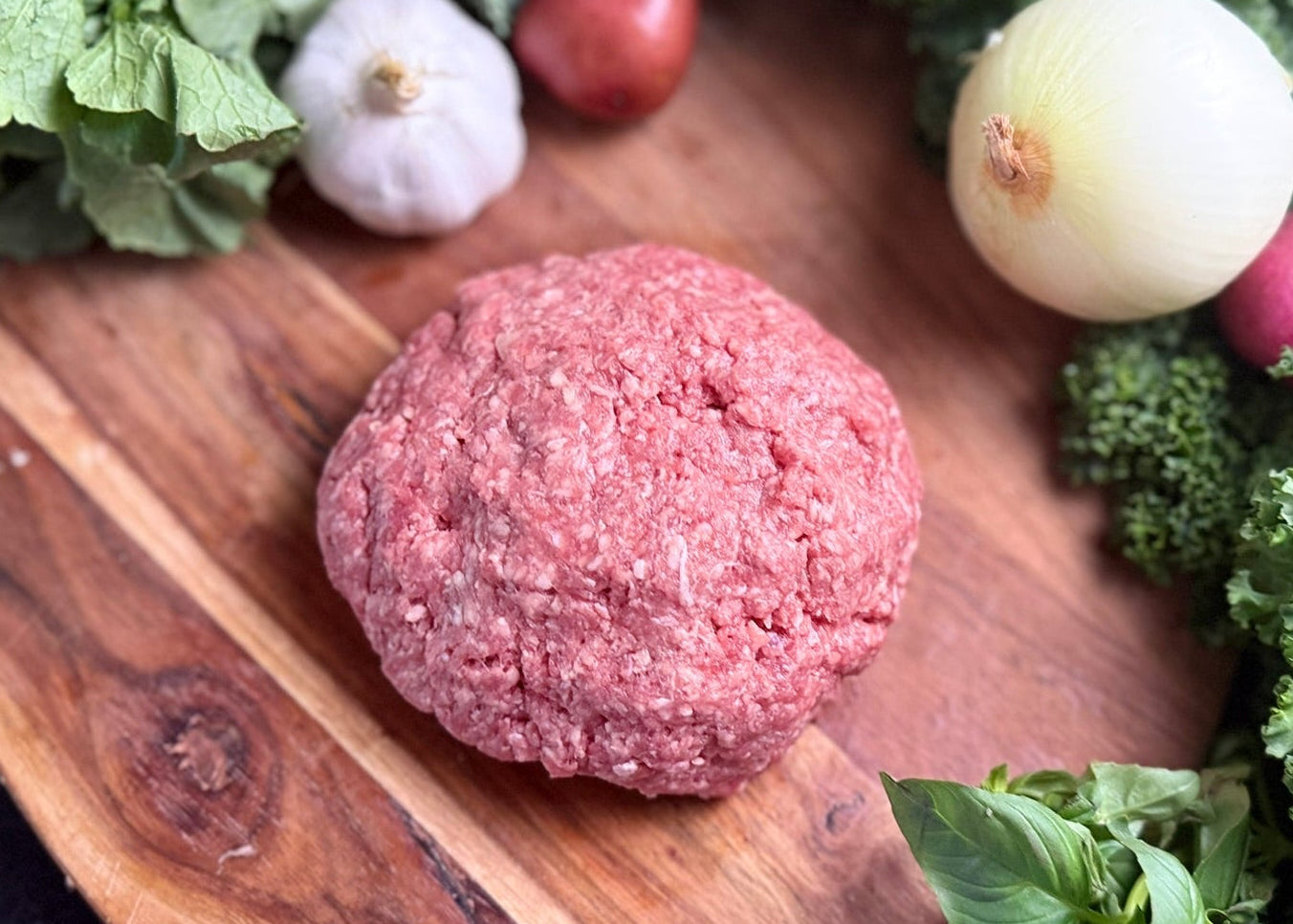 Raw ground meat patty on a wooden board with vegetables