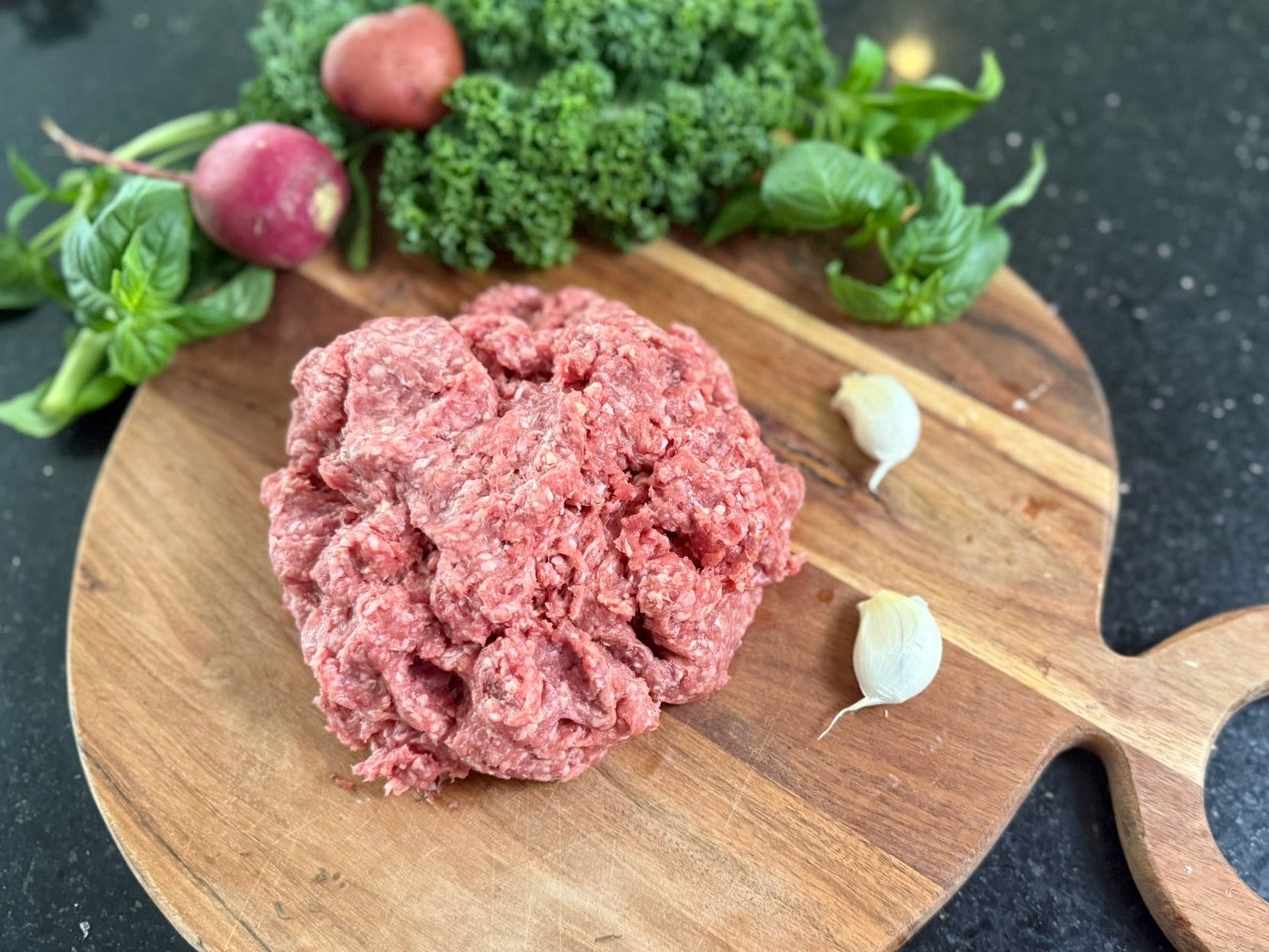 Raw ground meat on a wooden cutting board with vegetables in the background