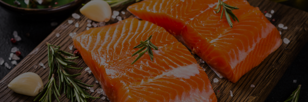 Salmon fillets on a wooden board with rosemary and garlic.