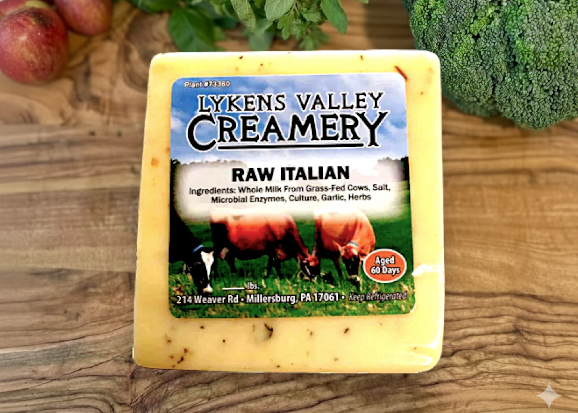 Block of Lyken's Valley Creamery Raw Italian cheese on a wooden surface with fruits and vegetables.