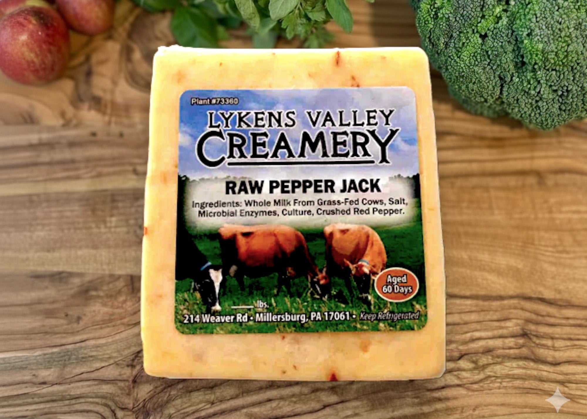 Lyken's Valley Creamery Raw Pepper Jack cheese on a wooden surface with vegetables in the background