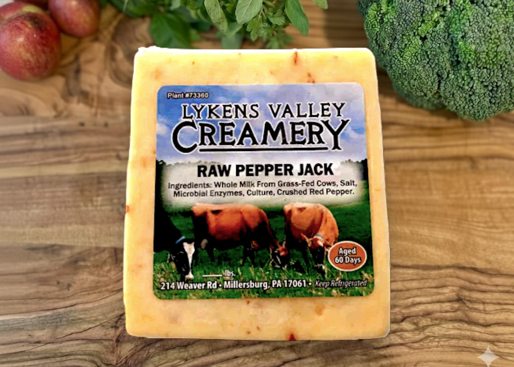 Lyken's Valley Creamery Raw Pepper Jack cheese on a wooden surface with vegetables in the background