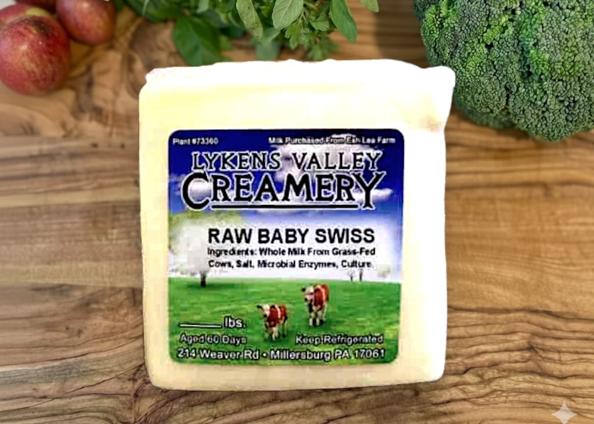 Block of raw baby Swiss cheese from Lykens Valley Creamery on a wooden surface with vegetables.