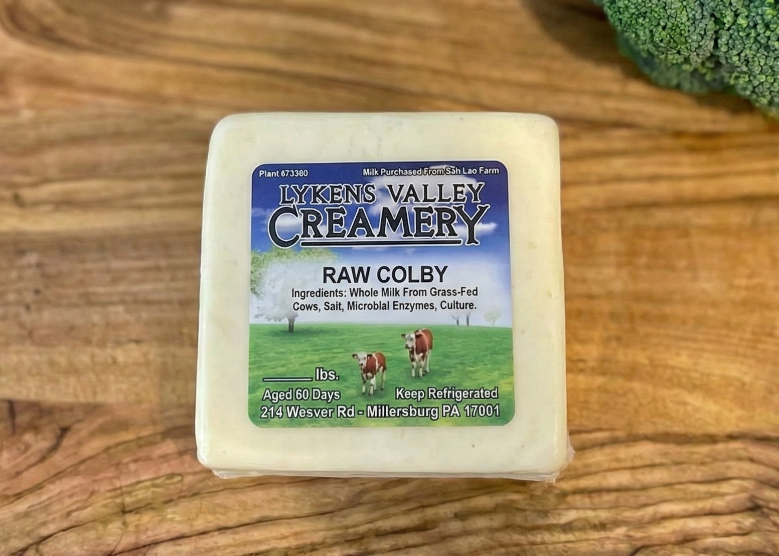 Block of Lykens Valley Creamery Raw Colby cheese on a wooden surface with vegetables.